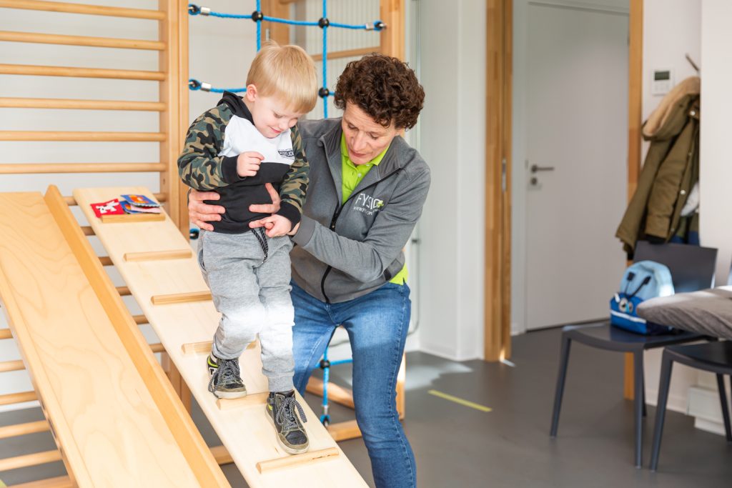 Kinderfysiotherapeut helpt een kindje naar beneden lopen in de oefenzaal