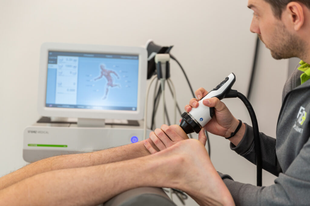 Therapeut voert de behandeling shockwave therapie uit bij iemand die hielspoor heeft