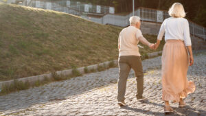 Oudere man en vrouw lopen hand in hand om erminderen van valrisico’s bij ouderen.